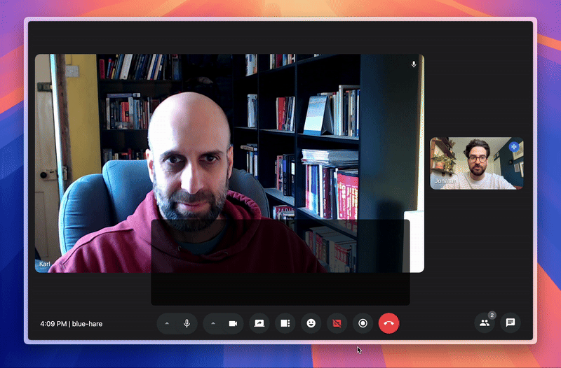 A video call between two men using a conferencing platform. The main speaker, named Karl, is seated in a room with bookshelves behind him, wearing a maroon hoodie. The second participant, Jonathan, appears in a smaller window, sitting in a well-lit room with plants in the background. The interface displays various call controls at the bottom, including microphone, camera, screen share, and hang-up buttons.