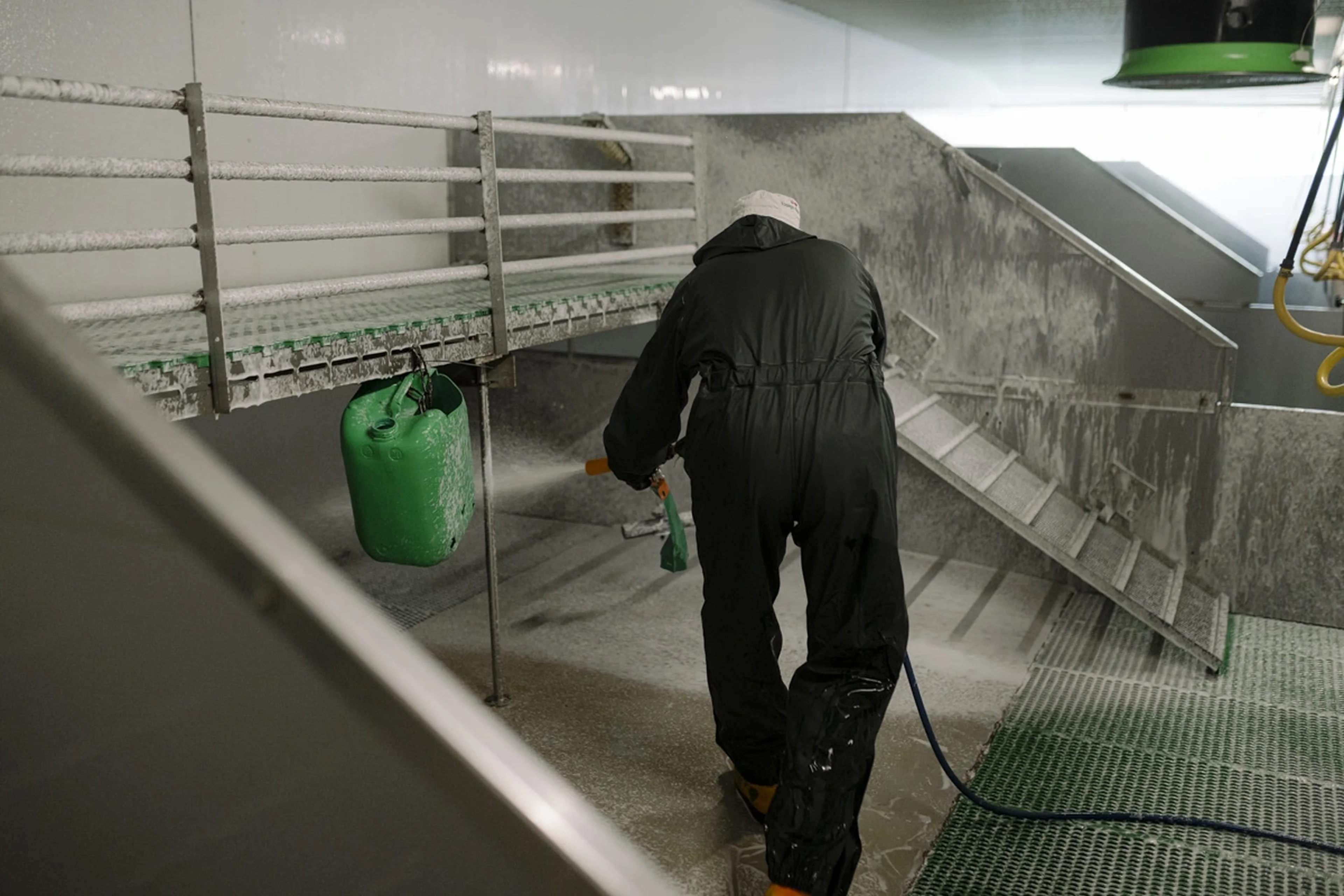 Person in protective gear cleaning a pig pen with a hose