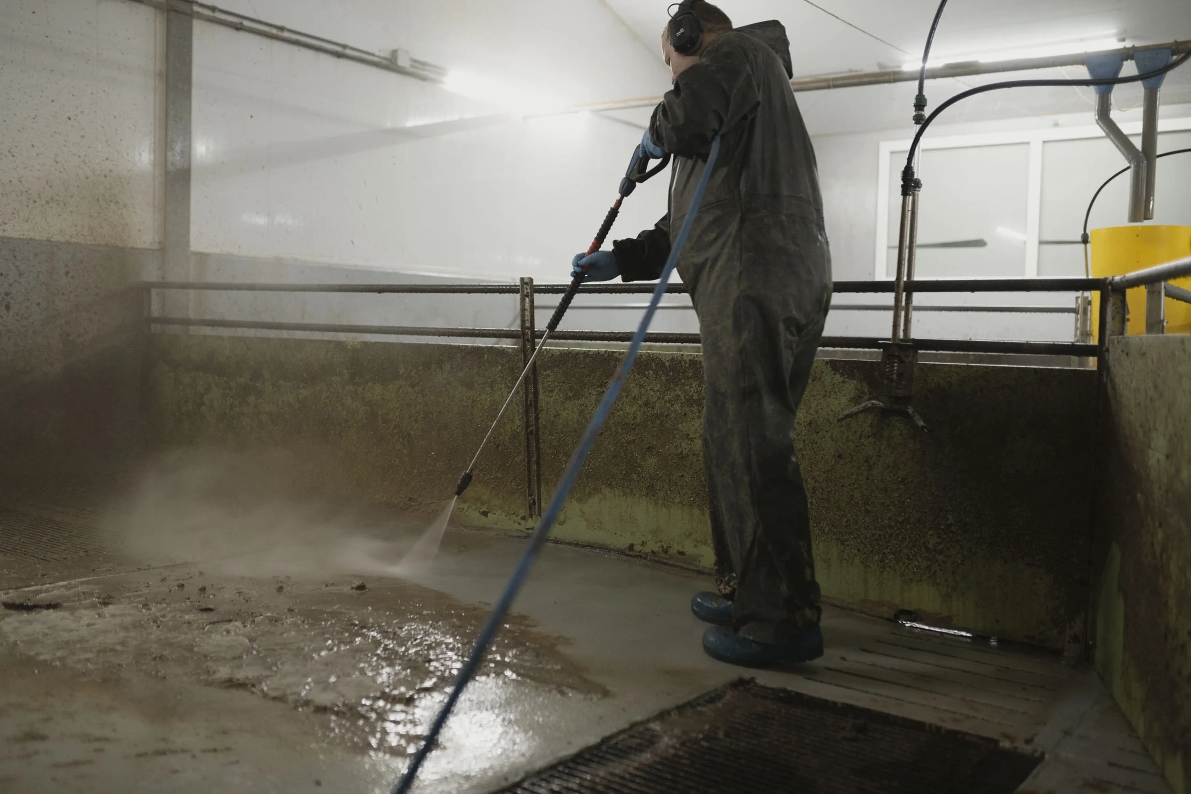 Person in protective gear pressure washing a dirty pig pen floor