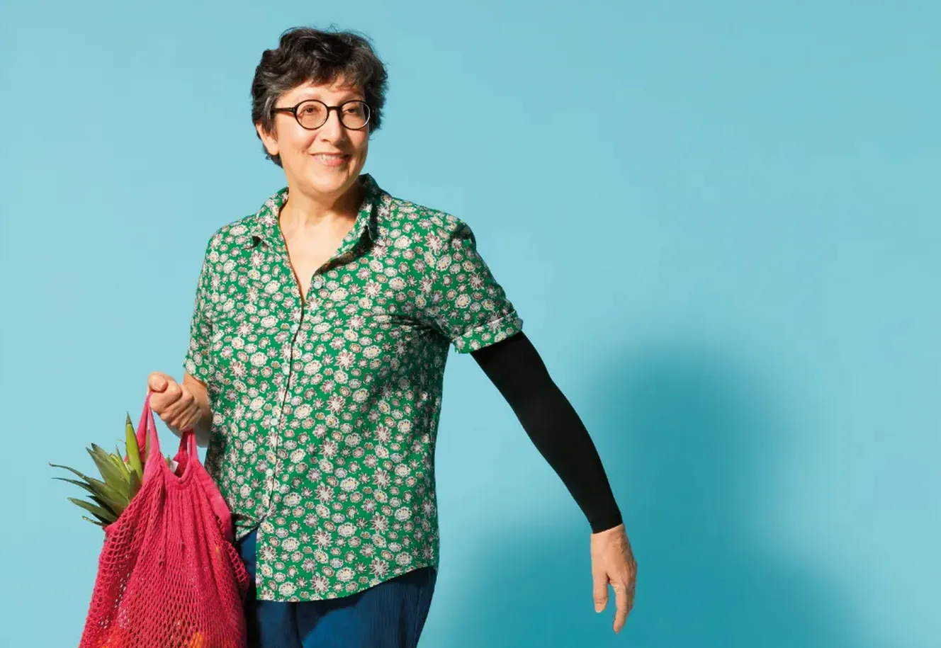 Frau trägt Tasche mit Einkäufen, buntes Hemd, kurze Haare, Brille, blauer Hintergrund