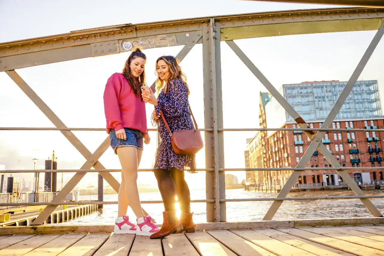 Zwei Frauen mit Kompressionsstrümpfen stehen nebeneinander auf einer Promenade im Hintergrund Wasser und Großstadt