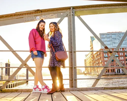 Zwei Frauen mit Kompressionsstrümpfen stehen nebeneinander auf einer Promenade im Hintergrund Wasser und Großstadt