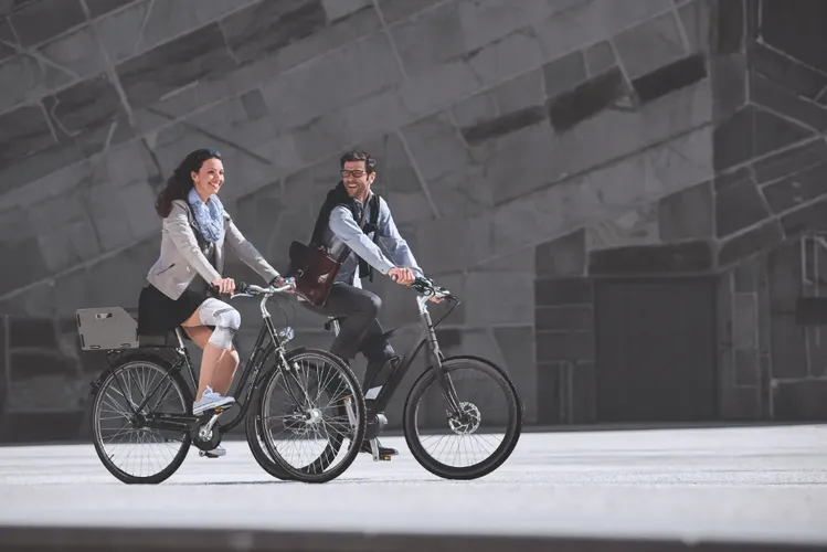 Mann und Frau mit Kniebandagen fahren Fahrrad, im Hintergrund eine graue Wand