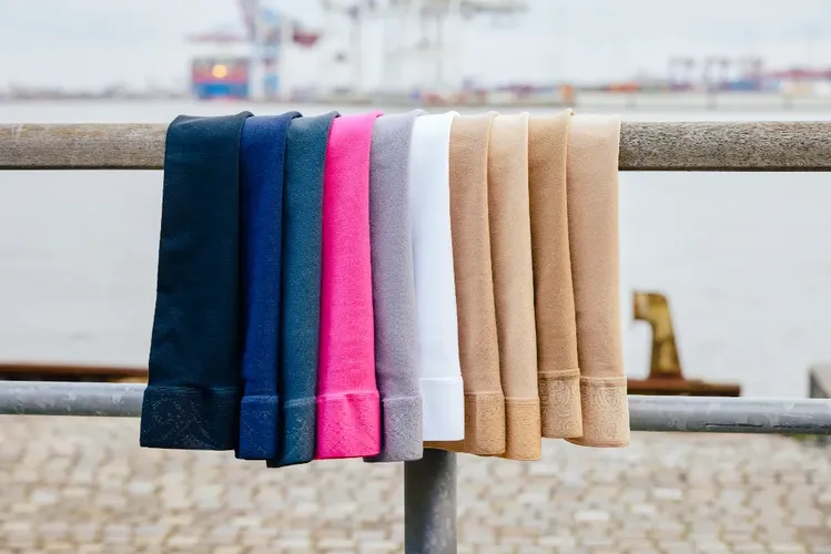 Kompressionsstrümpfe in verschiedenen Farben liegen über einem Bannister, im Hintergrund Wasser und ein Schiffshafen