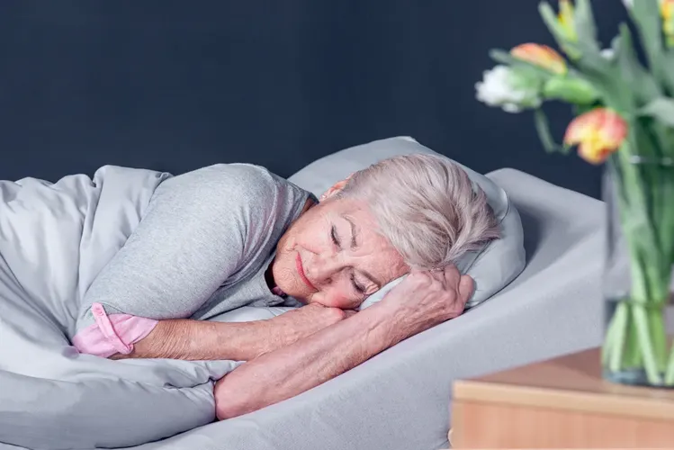 Ältere Frau liegt in einer VATI-Lagerung in einem erhöhten Bett mit geschlossenen Augen