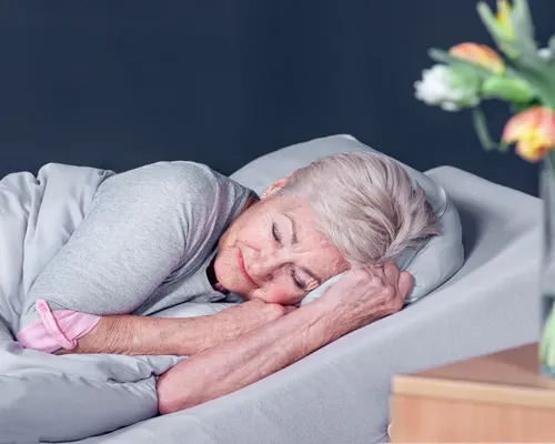Ältere Frau liegt in einer VATI-Lagerung in einem erhöhten Bett mit geschlossenen Augen
