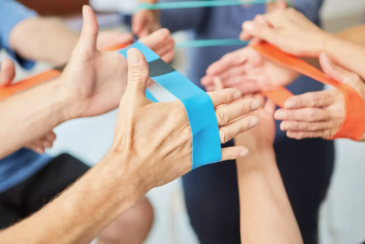 mehrere Personen machen Übung für Hände, wegen Schmerzen im Handgelenk, ziehen Sportband mit Händen auseinander
