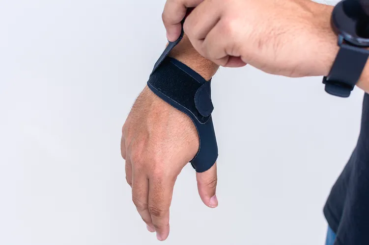 Mann mit Sehnenscheidenentzündung trägt Bandage an Hand und Daumen, schwarze Schiene