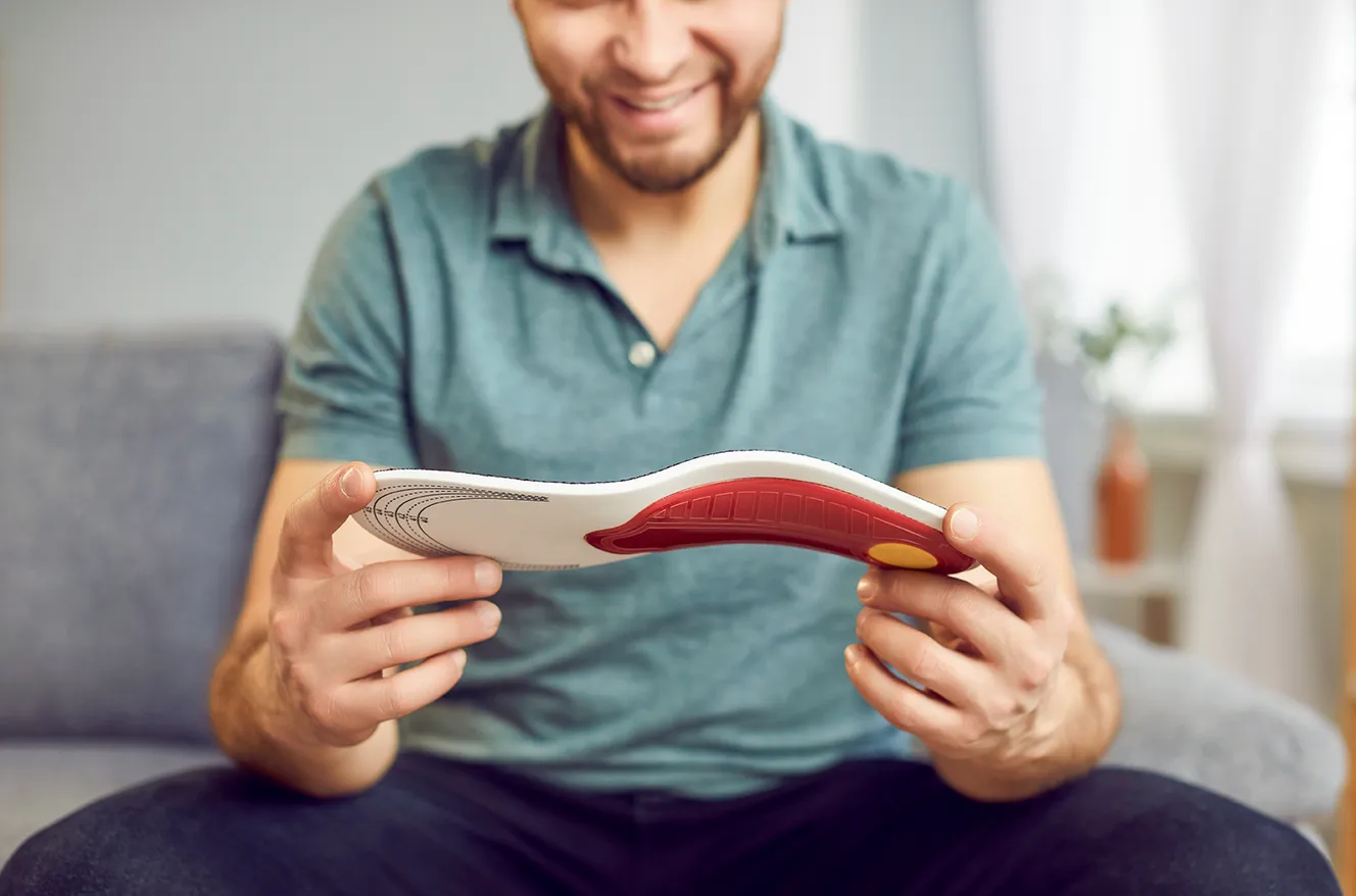 Plattfußsymptome, orthopädische Einlagen, Mann hält Einlage in Hand, Fußgewölbe sinkt ein