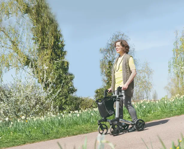 Frau mit Parkinson schiebt Rollator einen Abhang im Park herunter