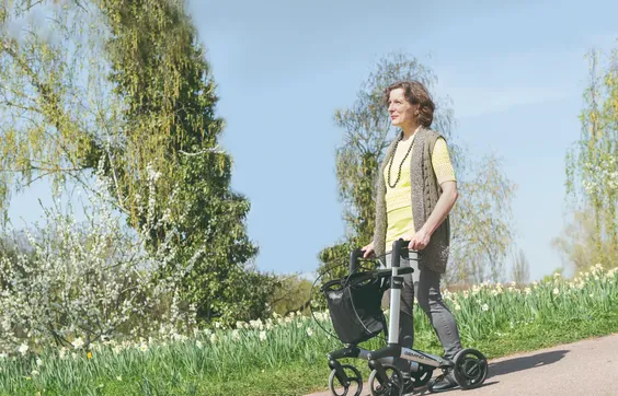 Frau mit Parkinson schiebt Rollator einen Abhang im Park herunter