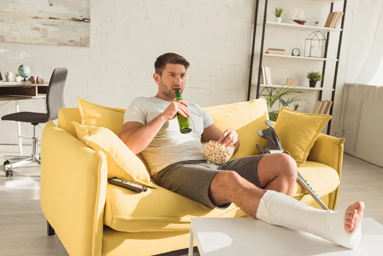 Gips oder Orthese, Mann zuhause mit Gips und Krücken,  Knochenbruch