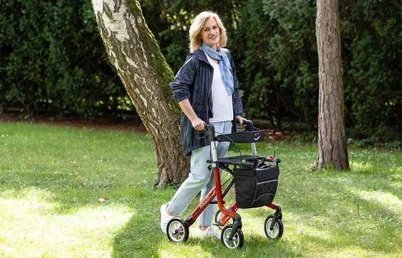 Frau mit Parkinson mit Rollator auf grüner Wiese, im Hintergrund Bäume, Charcot-Marie-Tooth-Syndrom