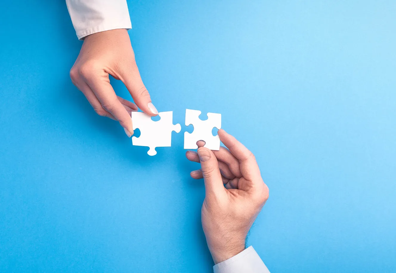 zwei Hände halten passende Puzzleteile aneinander, blauer Hintergrund