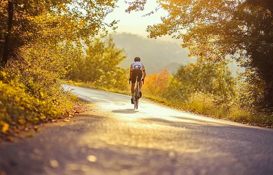 Mann in Sportkleidung mit Schmerzen im Gesäß fährt Fahrrad auf Straße, Bäume an der Seite