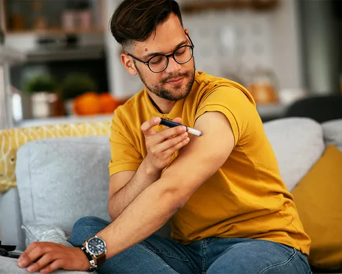 Mann mit Hyperglykämie, spritzt sich Insulin, sitzt auf Sofa, gelbes T-Shirt