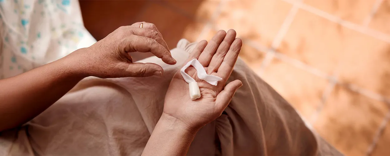 Person hält einen Analtampon mit Rückholband in der offenen Hand, die andere Hand greift danach.