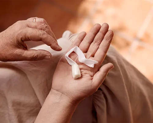Person hält einen Analtampon mit Rückholband in der offenen Hand, die andere Hand greift danach.