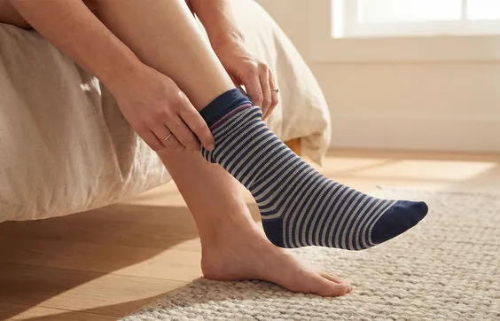 Unterschenkel und Füße einer Frau im Schlafzimmer, die sich einen Kompressionsstrumpf anzieht
