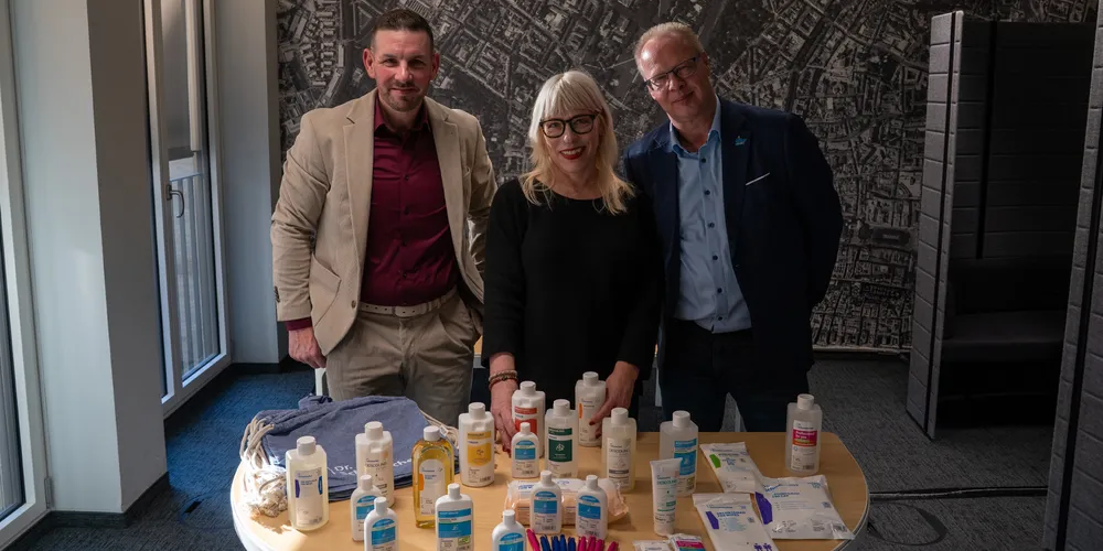 joviva-Mitarbeiterin Karin Pütz mit zwei Mitarbeitern der Dr. Schumacher GmbH in einem modernen Bürogebäude vor einem Tisch mit Hygieneprodukten