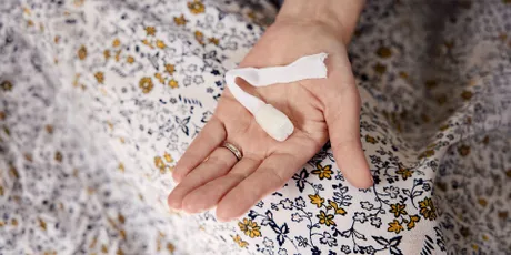 Hand, die einen Analtampon mit Rückholband vor einem geblümten Stoff hält.