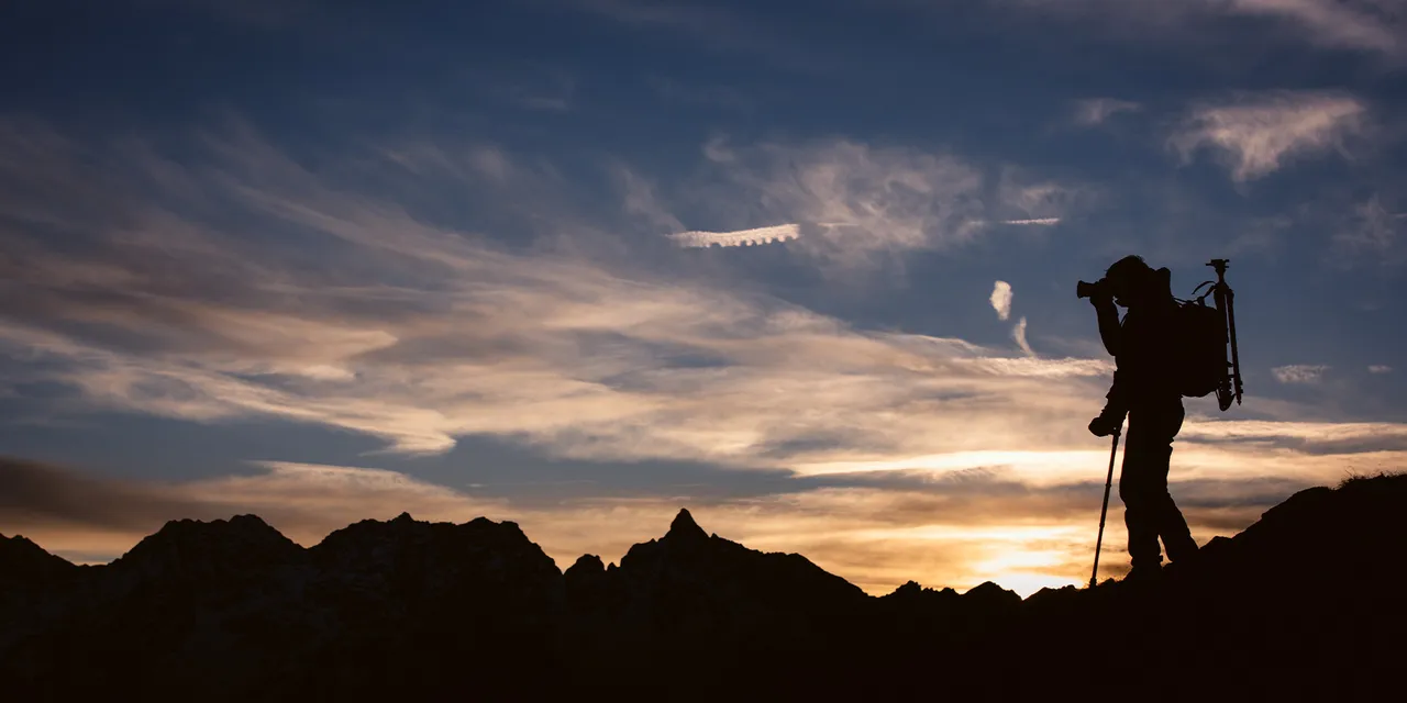 Schwarze Silhouette eines Mannes mit Gehstock und SAFETYFOOT-Gummikapsel von Patrick Mayer, der in einer Berglandschaft bei Sonnenuntergang fotografiert