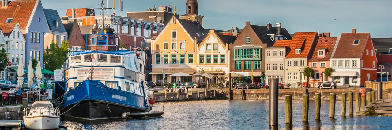 Eine farbenfrohe Szene am Wasser mit vor Anker liegenden Booten, lebhaften Gebäuden und einem klaren Himmel im Hintergrund.