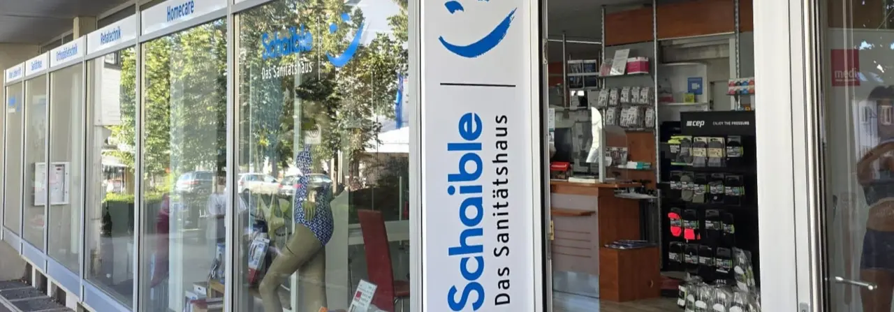 Storefront of a medical supply store, "Schaible Das Sanitätshaus," with products displayed and signage above glass windows.