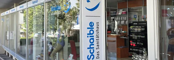 Storefront of a medical supply store, "Schaible Das Sanitätshaus," with products displayed and signage above glass windows.