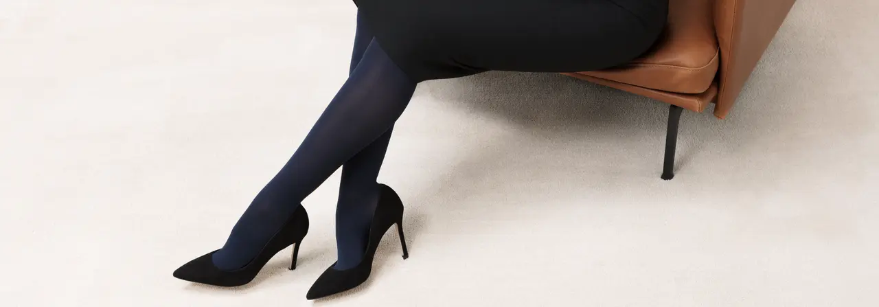 Beine in dunklen Kompressionsstrümpfen in schwarzen High-Heels auf beigem Teppich
