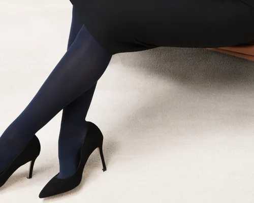 Beine in dunklen Kompressionsstrümpfen in schwarzen High-Heels auf beigem Teppich