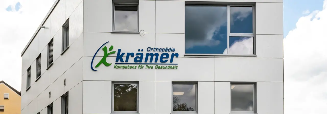 Weißes Gebäude des Sanitätshauses Orthopädie Krämer, im Hintergrund blauer Himmel