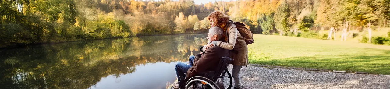 Schlaganfall-Folgen, Mann im Rollstuhl mit Angehöriger im Park, Rehabilitation
