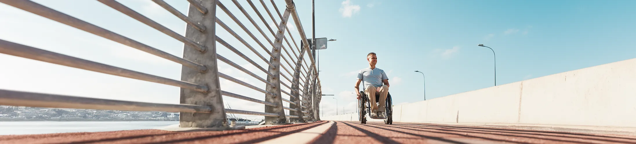 Rollstuhl auf Rezept, Betroffener fährt strahlend über eine Brücke, Mobilität, Lebensfreude