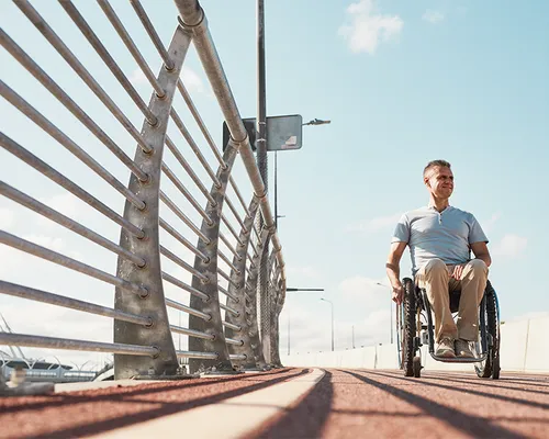 Rollstuhl auf Rezept, Betroffener fährt strahlend über eine Brücke, Mobilität, Lebensfreude