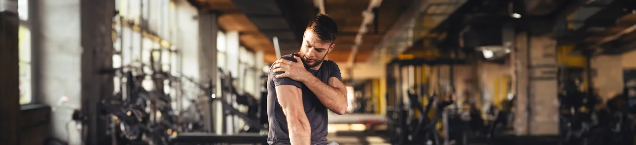 Omarthrose Schulter, Mann in Fitnessstudio hält sich die schmerzende Schulter, Gelenkgeräusche