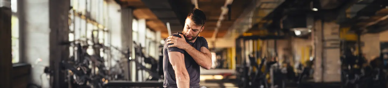 Omarthrose Schulter, Mann in Fitnessstudio hält sich die schmerzende Schulter, Gelenkgeräusche