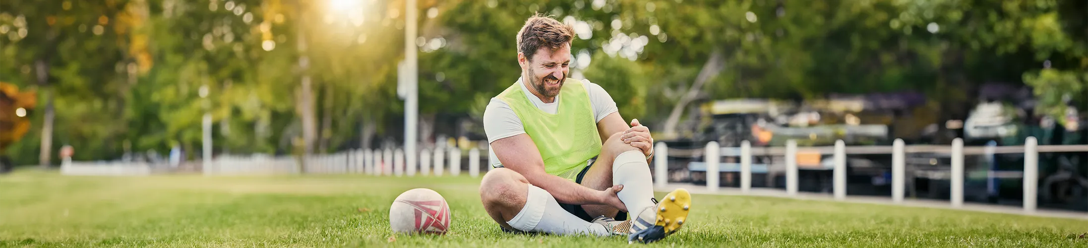 Kreuzbandriss, Fußballer sitzt auf Rasen, geschwollenes Knie, starke Schmerzen