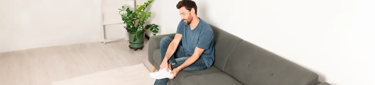 Plantarfasziitis, Mann auf Sofa hält sich Ferse, chronische Entzündung, Fersenbein