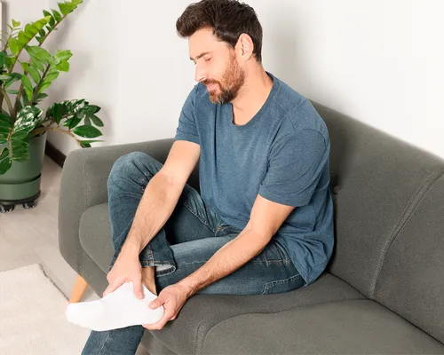 Plantarfasziitis, Mann auf Sofa hält sich Ferse, chronische Entzündung, Fersenbein