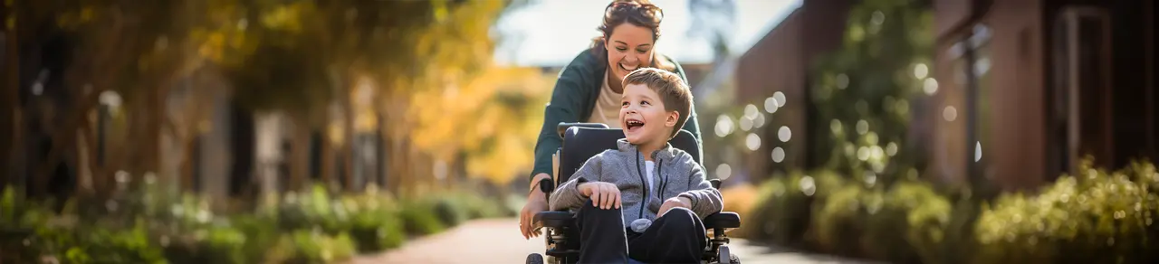 Infantile Cerebralparese, lachender kleiner Junge im Rollstuhl mit Mutter, Probleme mit der Motorik, nicht fortschreitende Hirnschädigung