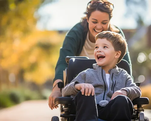 Infantile Cerebralparese, lachender kleiner Junge im Rollstuhl mit Mutter, Probleme mit der Motorik, nicht fortschreitende Hirnschädigung