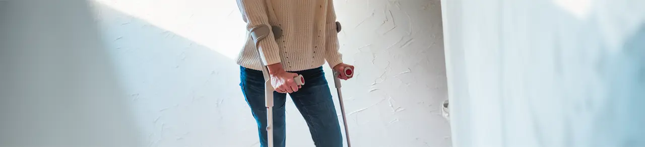 Mittelfußbruch, Frau in Flur mit Krücken, Unterarmgehstützen, Bruch verbunden mit Schwellungen und Belastungsschmerzen