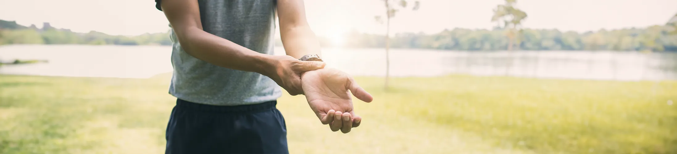 Schmerzen Handgelenk, Mann in Sportkleidung fasst sich an Handgelenk,  Schmerztherapie und Bewegungstherapie