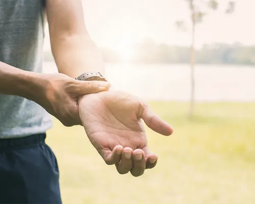 Schmerzen Handgelenk, Mann in Sportkleidung fasst sich an Handgelenk,  Schmerztherapie und Bewegungstherapie