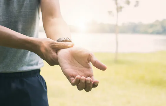 Schmerzen Handgelenk, Mann in Sportkleidung fasst sich an Handgelenk,  Schmerztherapie und Bewegungstherapie