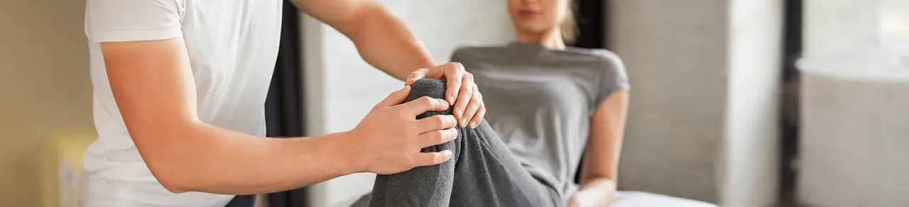 Patellaspitzensyndrom, Arzt legt Hände an Knie von Betroffener, schmerzhafter Reizzustand der Patellasehne, entsteht durch Fehlbelastung