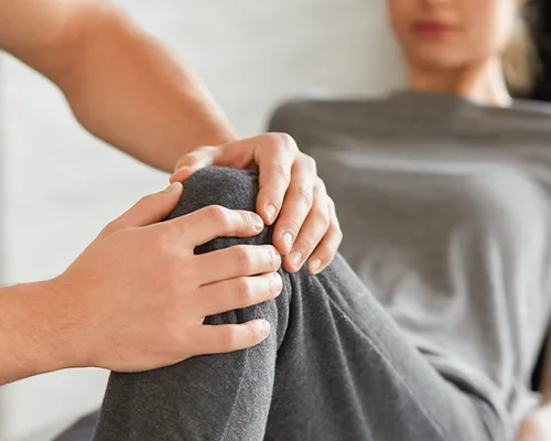 Patellaspitzensyndrom, Arzt legt Hände an Knie von Betroffener, schmerzhafter Reizzustand der Patellasehne, entsteht durch Fehlbelastung