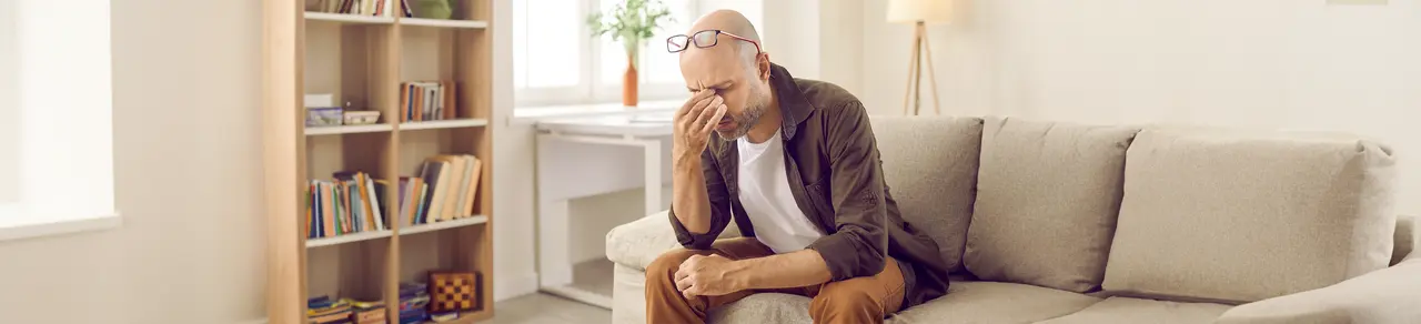 Schädel-Hirn-Trauma, Mann zu Hause auf Sofa fasst sich an die Augen, Kopfschmerzen, Übelkeit, Schwindel