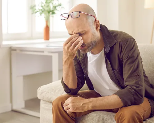 Schädel-Hirn-Trauma, Mann zu Hause auf Sofa fasst sich an die Augen, Kopfschmerzen, Übelkeit, Schwindel